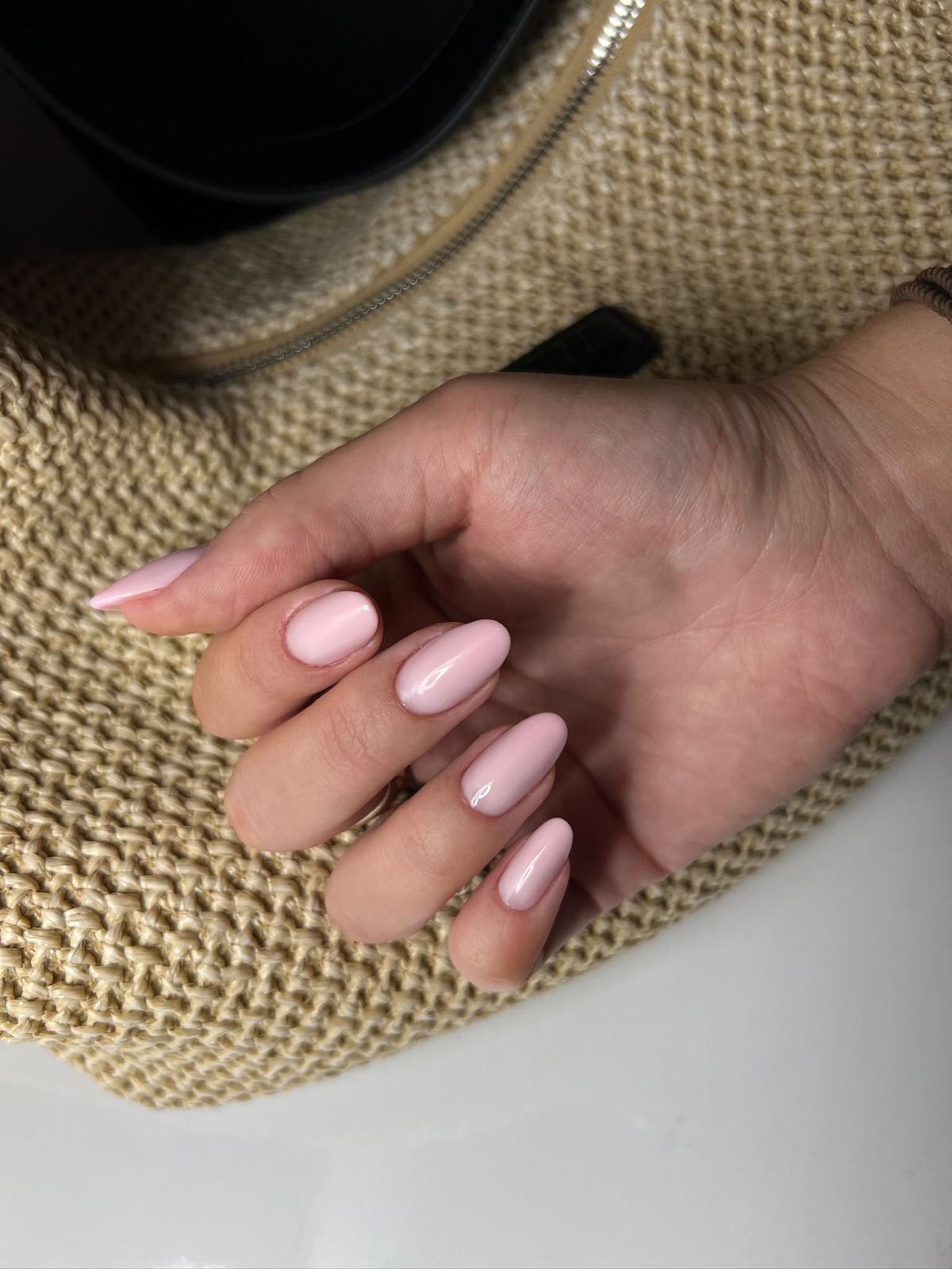 Soft-pink Nägel auf einer Strohtasche